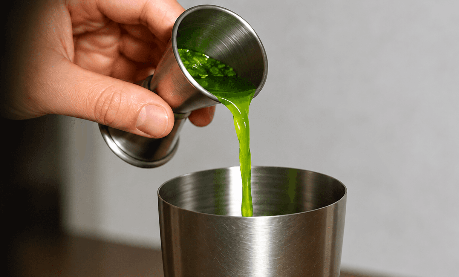 A green measure being poured during drink preparation